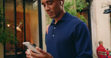 Muž se sluchátky AirPods drží iPhone na ulici