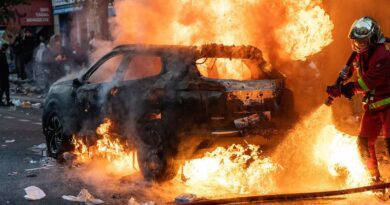 Hasič hasí hořící auto v pařížské ulici během protestů