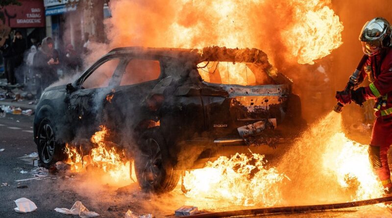 Hasič hasí hořící auto v pařížské ulici během protestů