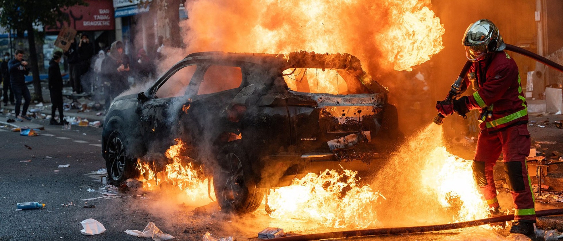Hasič hasí hořící auto v pařížské ulici během protestů
