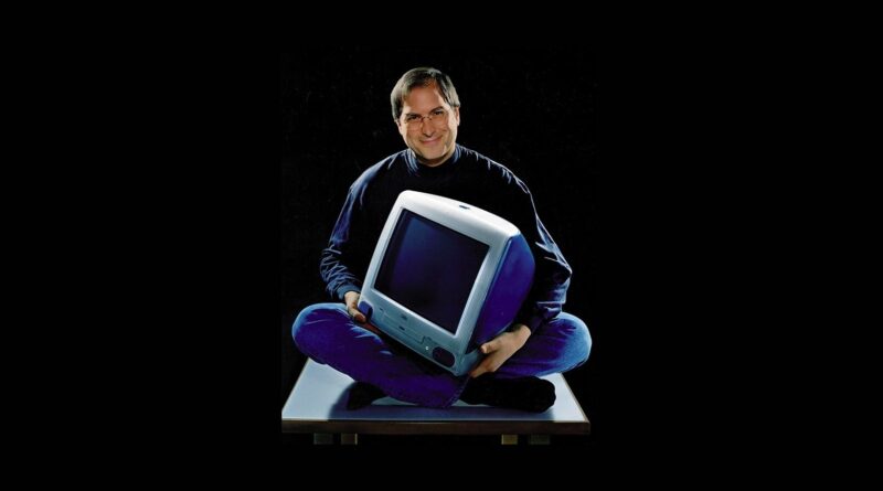 Steve Jobs sedící se zkříženýma nohama a původním počítačem iMac v klíně